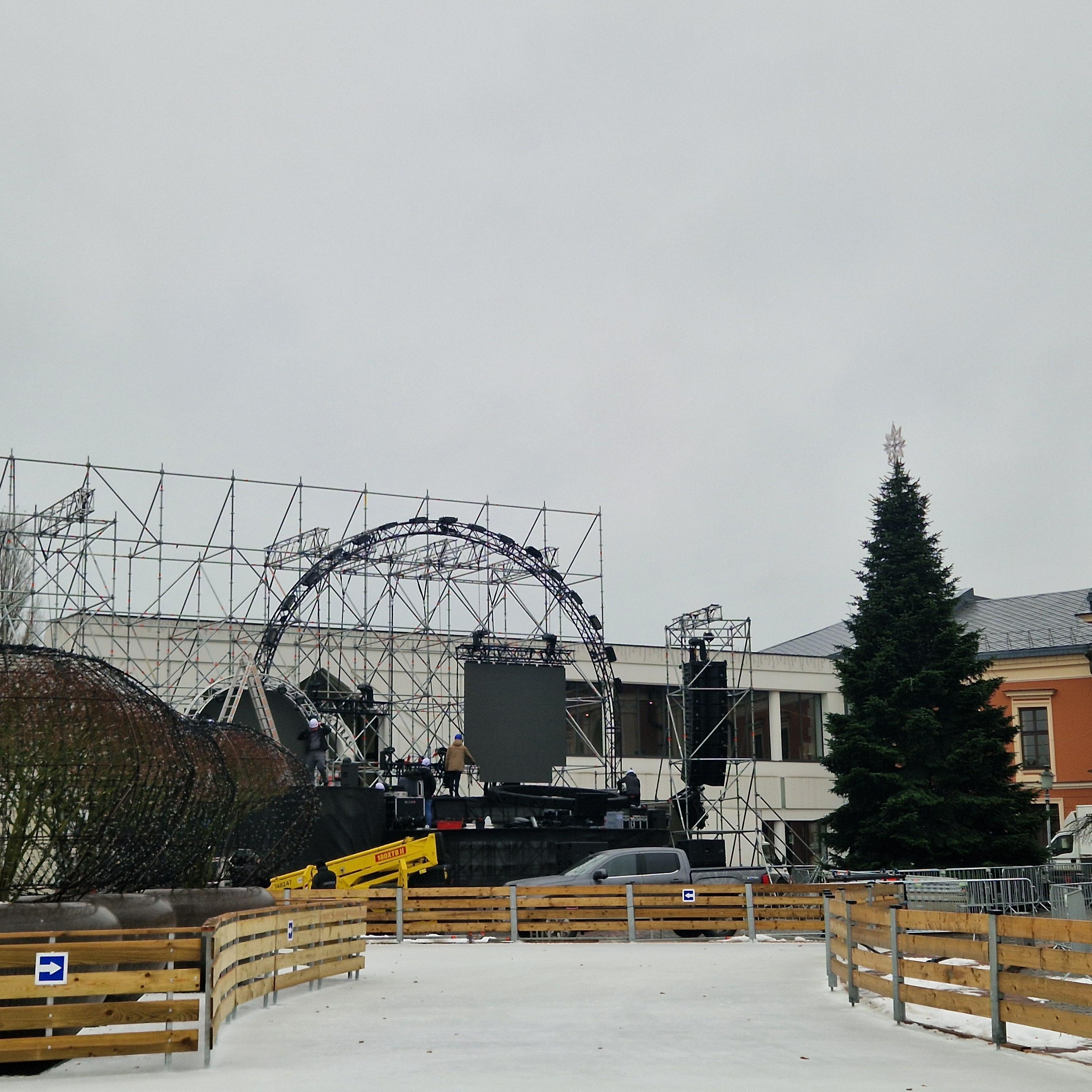 Veiksmas: penktadienį Teatro aikštėje tebevyko pasiruošimo įžiebimo šventei darbai, buvo ruošiama scena, puošiama eglutė.