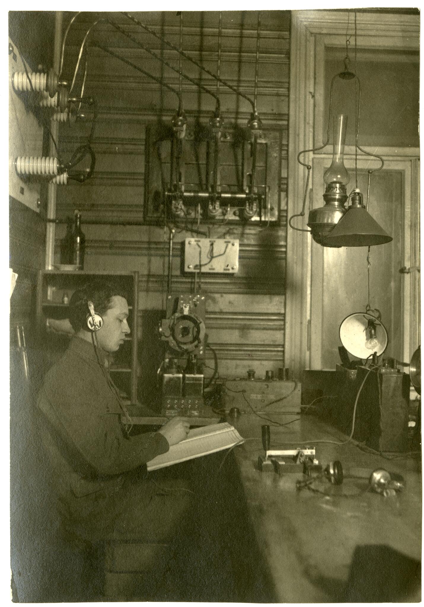 Kauno radijo stoties vienoje iš patalpų nežinomas asmuo su ausinėmis užrašo priimamą radiotelegrafinį pranešimą. 1920 m.