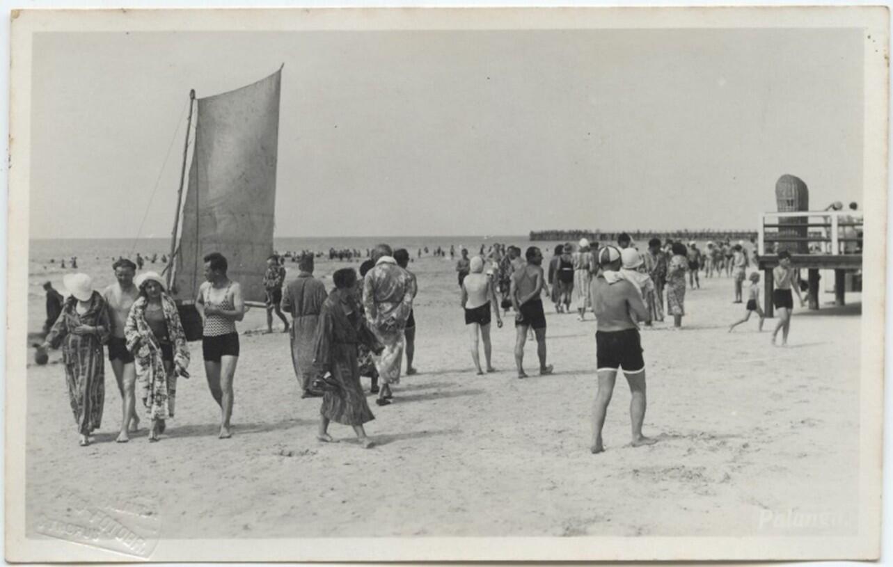 Palangos pliažas, 1936 m. Igno Stropaus fotoatvirukas. Lietuvos nacionalinio muziejaus rinkinys. Pirmame plane – vasarotojai su chalatais, už jų – žvejų burvaltės burė, o dešinėje antrame plane – Pajūrio halės prieangyje stovi pintas paplūdimio krėslas.