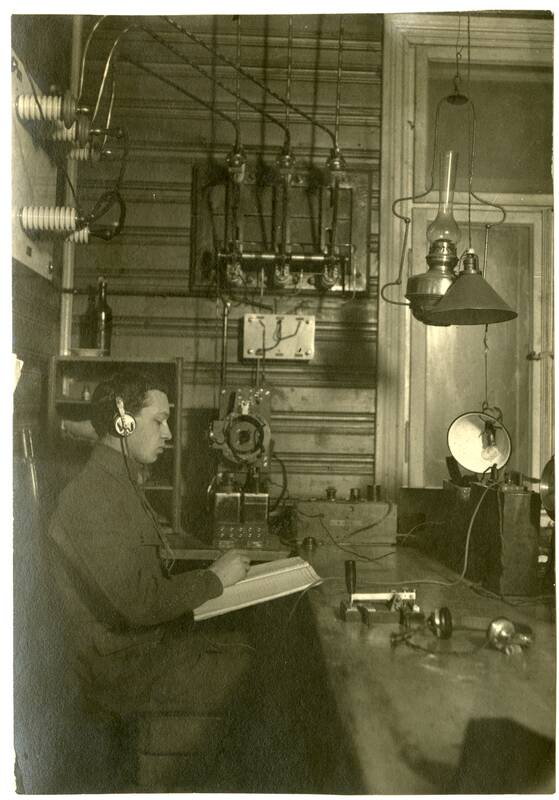 Kauno radijo stoties vienoje iš patalpų nežinomas asmuo su ausinėmis užrašo priimamą radiotelegrafinį pranešimą. 1920 m.